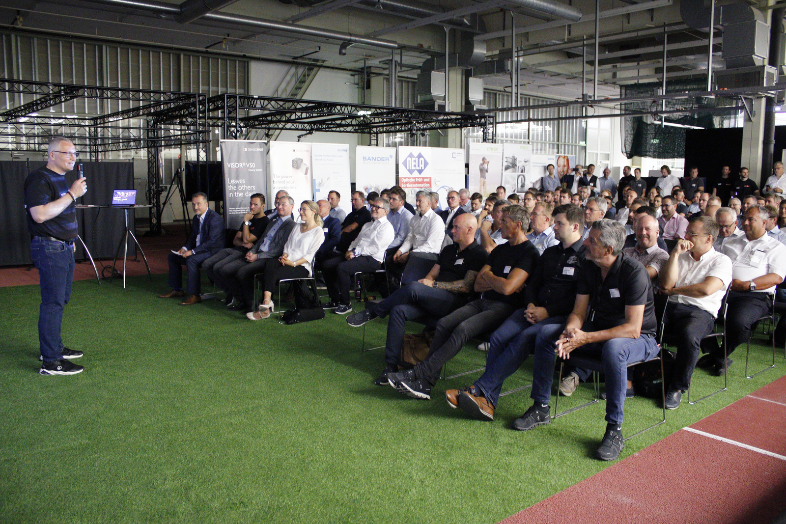 Ein Mann mit Mikrofon steht vor sitzendem und stehendem Publikum