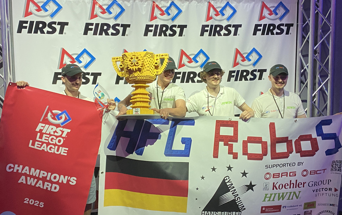 Vier junge Männer mit einem gelben Pokal aus Legosteinen und der Teamfahne