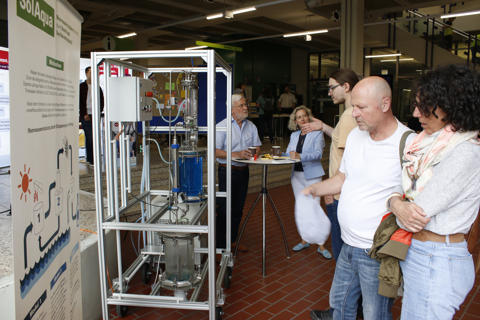 Menschen stehen vor einem Plakat und einer Entsalzungsanlage
