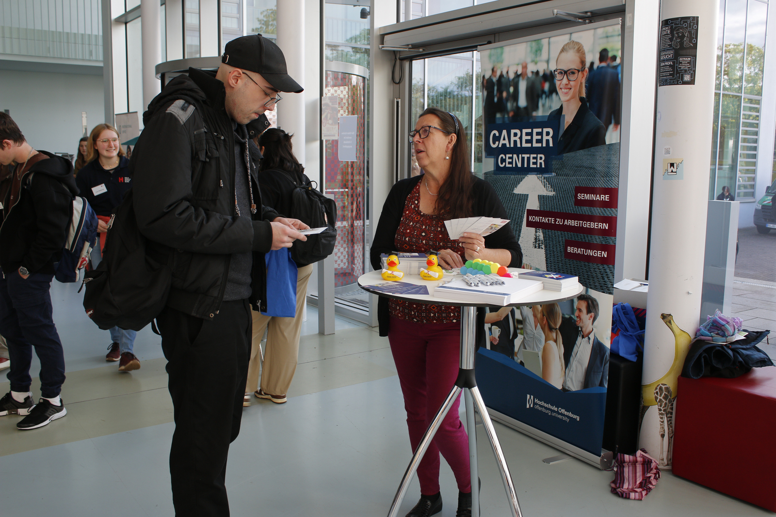 Ein Frau berät einen Mann mit Schirmmütze am Infotisch des Career Centers