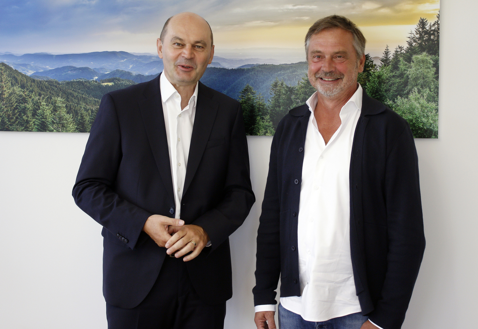 Zwei Männer stehen vor einem Schwarzwaldfoto und schauen in die Kamera