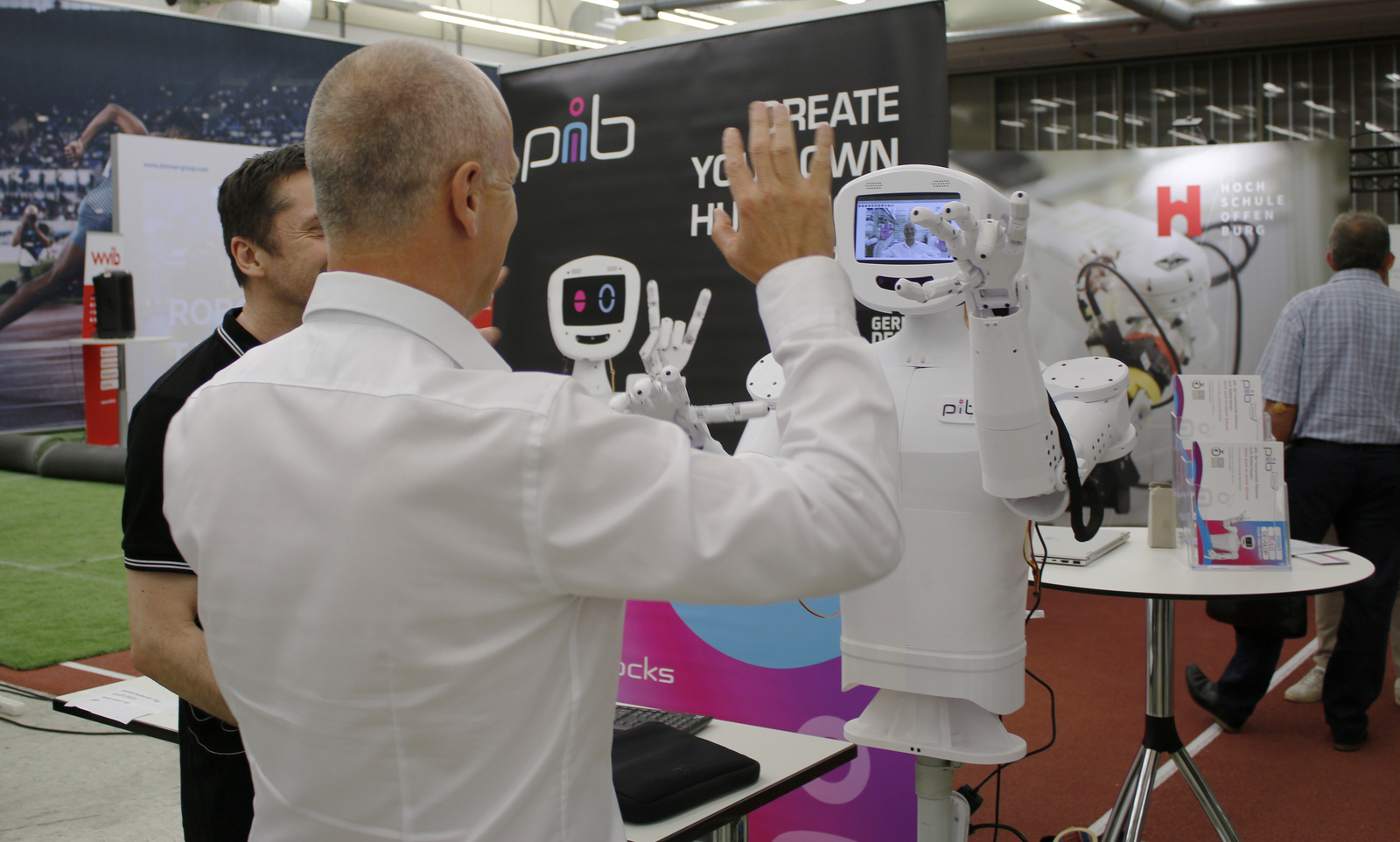 Ein Mann hebt die Hände und ein humanoider Roboter mit einem Kamerabild im Kopf macht es ihm nach