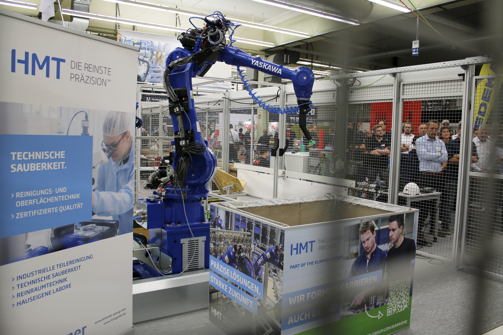 Menschen Stehen außerhalb einen Käfigs und beobachten den Roboterarm darin