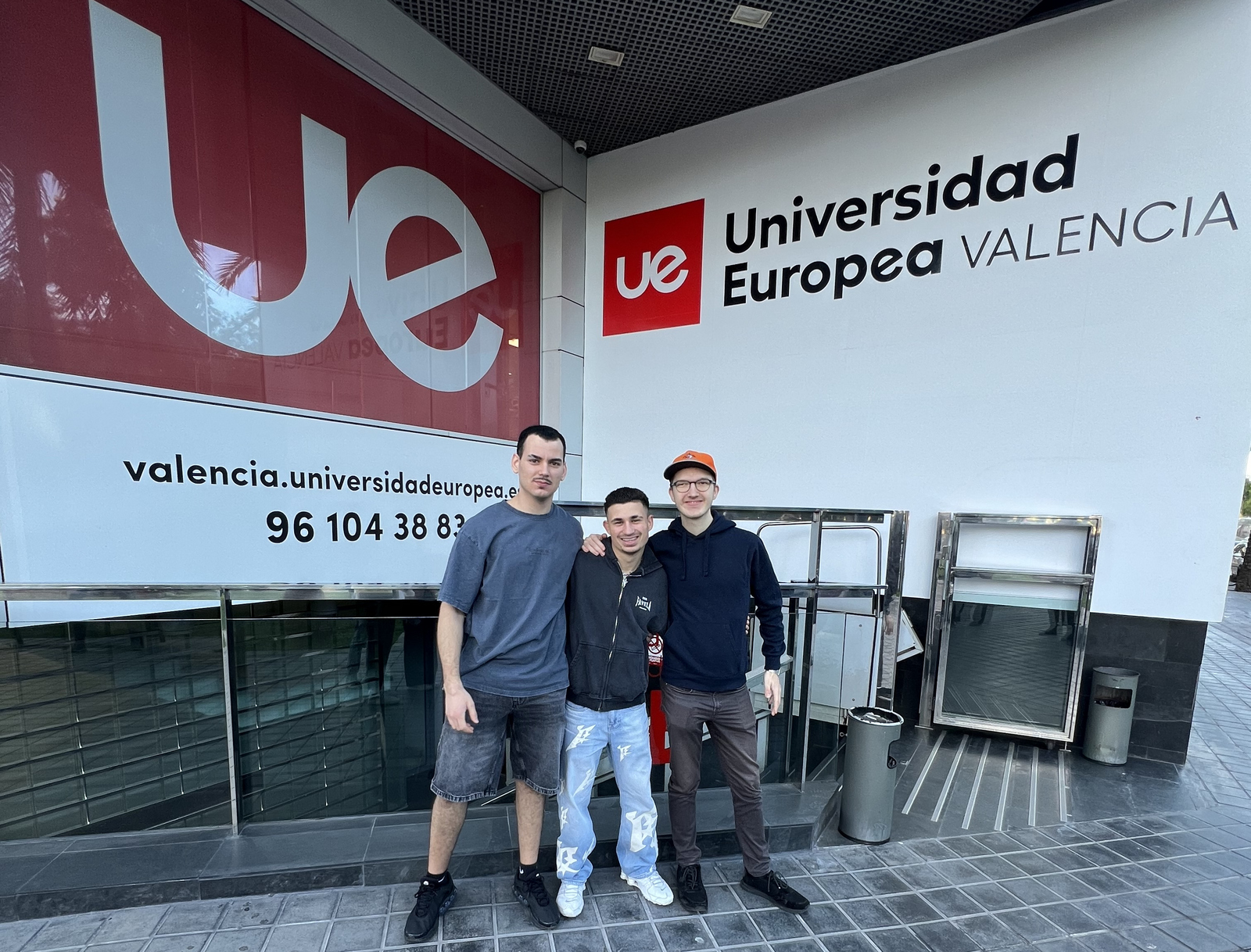 Drei junge Männer stehen Arm in Arm vor einer Wand mit der Aufschrift Universidad Europea Valencia
