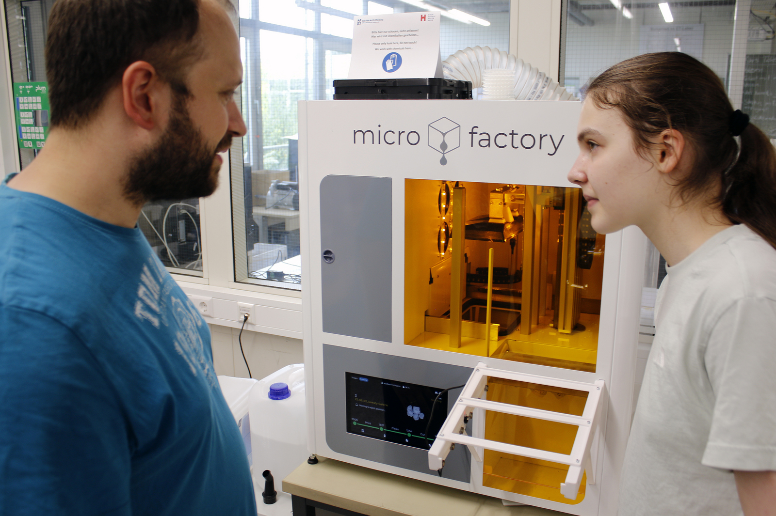 Ein Mädchen und ein Mann stehen an einem 3D-Kunstharz-Drucker 