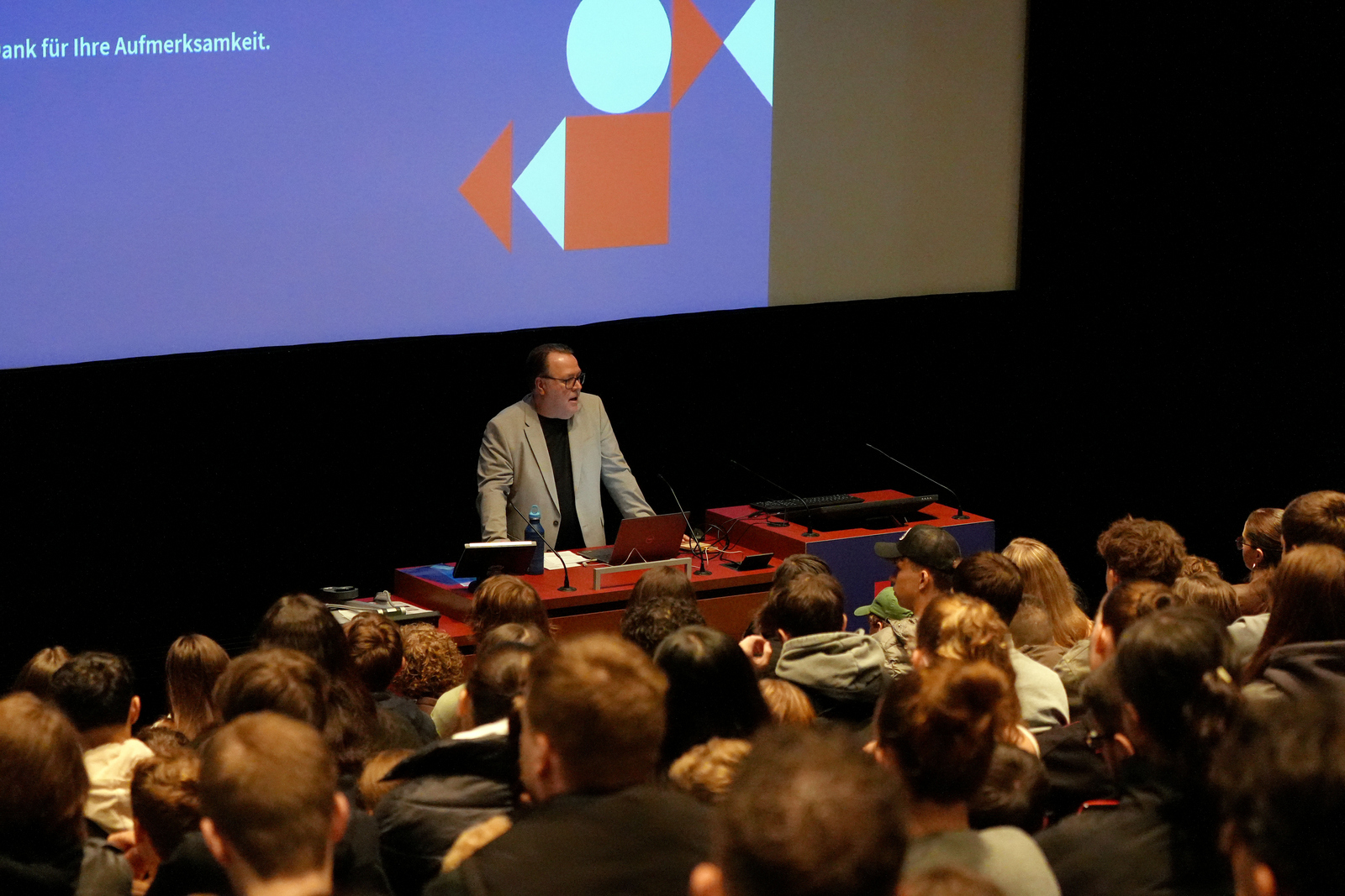 ein Mann steht am Rednerpult vor sitzenden Studierenden in einem Hörsaal