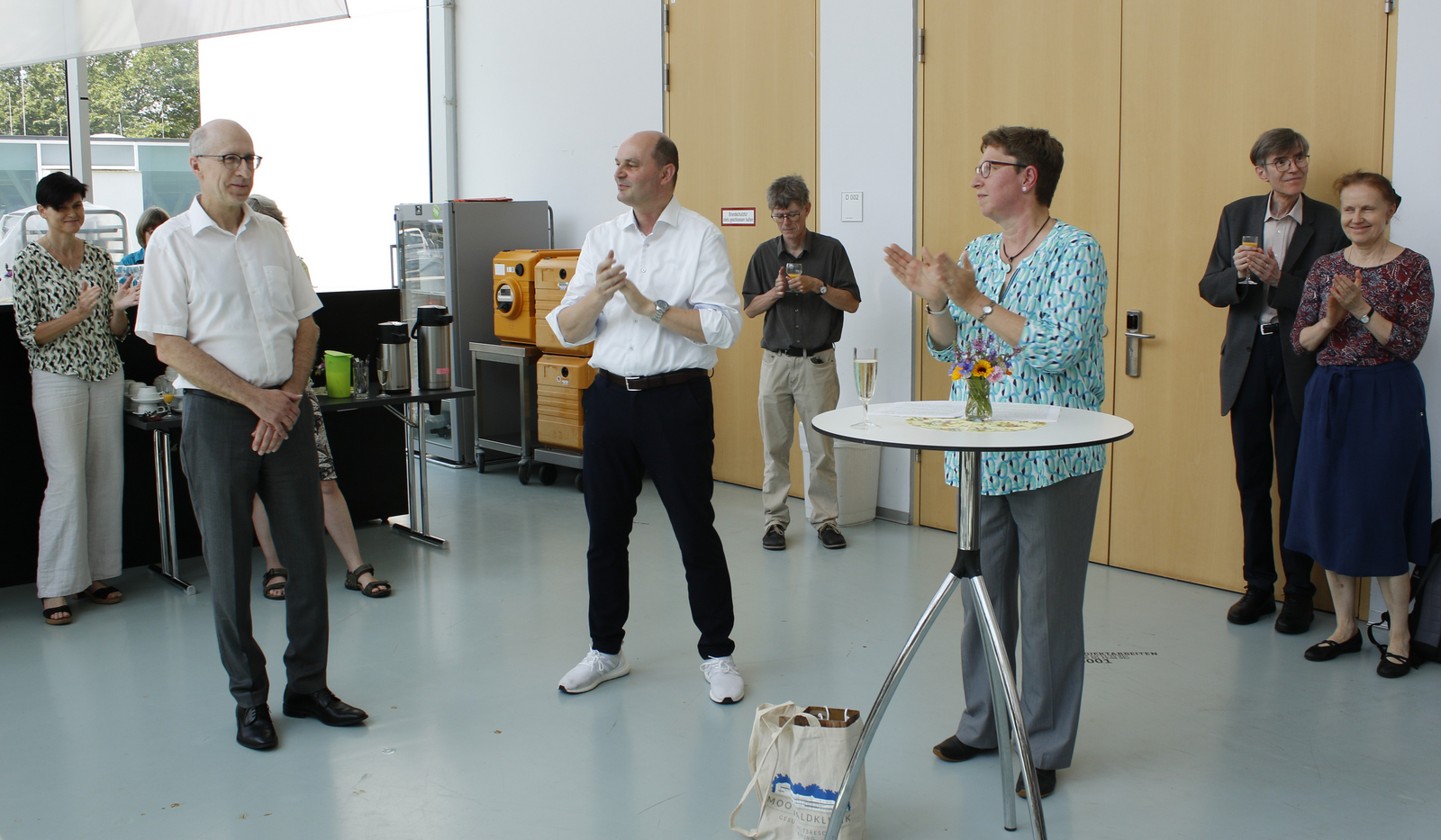 Andreas Christ, Stephan Trahasch und Elke Mackensen stehen in einem Halbkreis um eine Stehtisch im Foyer von Gebäude D und um sie herum weitere Menschen