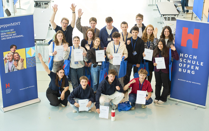 Gruppenfoto der zwischen zwei Roll-ups knieenden und stehenden Teilnehmenden mit Urkunden