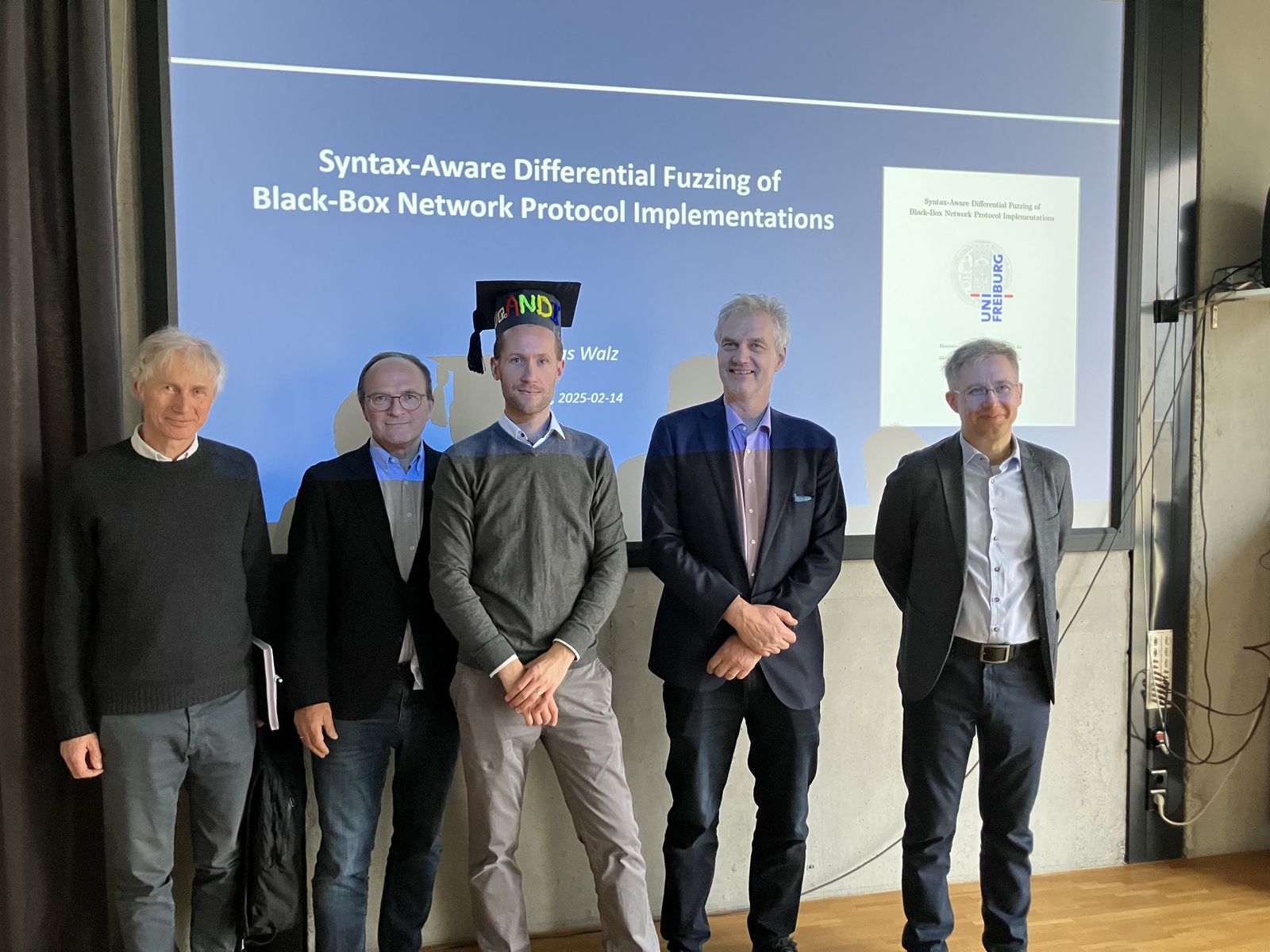 Andreas Walz with 4 members of the examination board in front of a whiteboard shwoing his presentation