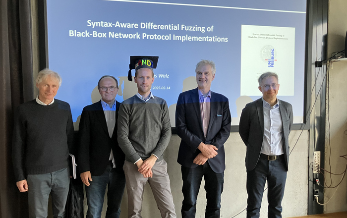 Andreas Walz with 4 members of the examination board in front of a whiteboard shwoing his presentation