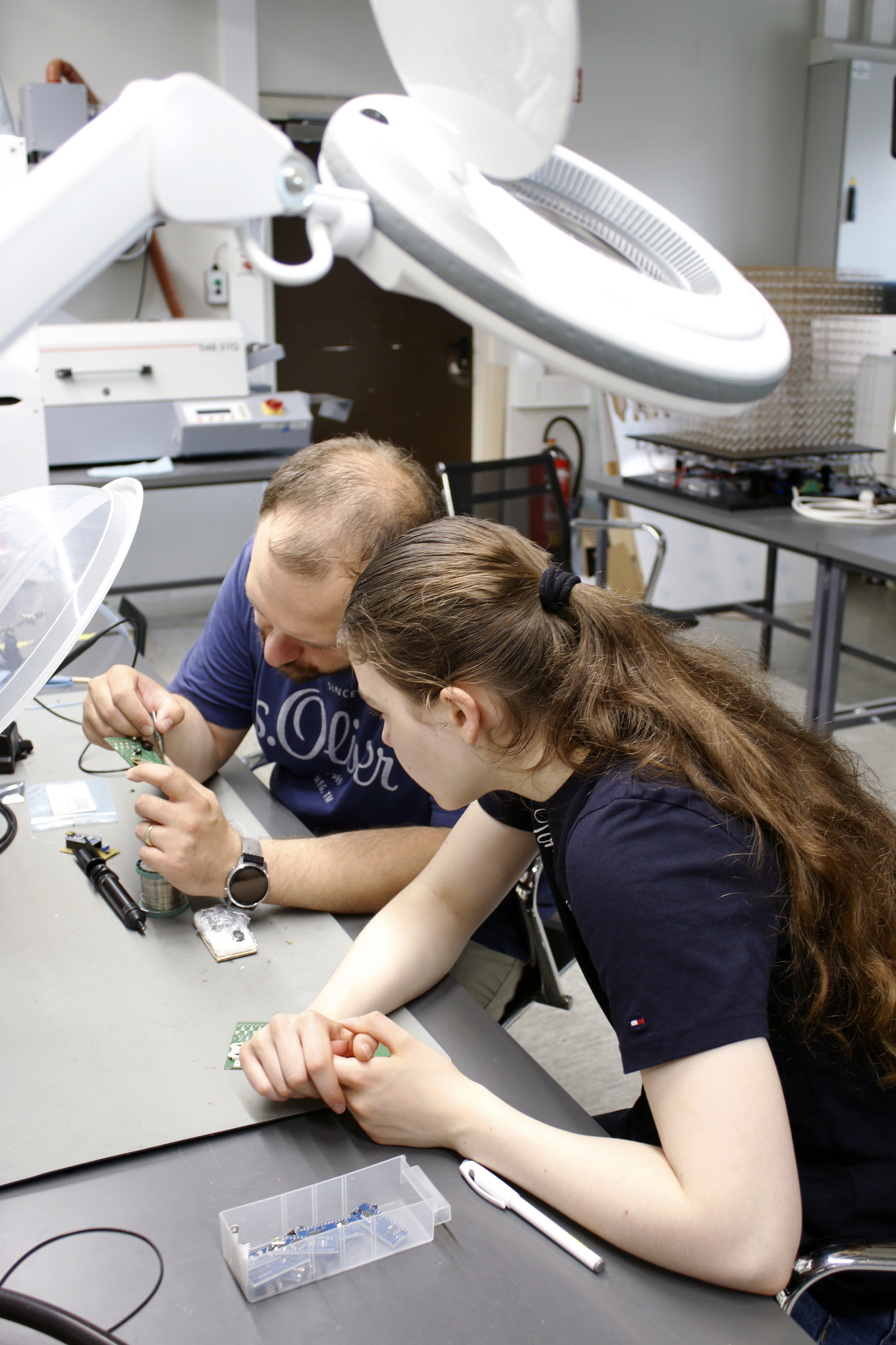 Ein Mädchen und ein Mann sitzen an einem Tisch und arbeiten an einer Platine