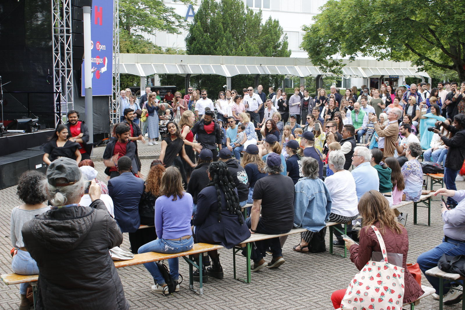 ein Gruppe schwarz-rot gekleideter menschen tanzt vor den sitzenden Zuschauerinnen und Zuschauern. 