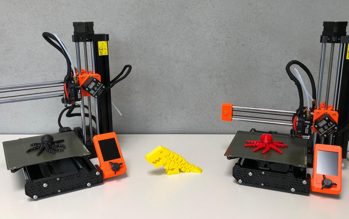 Zwei 3D-Drucker und einige mit diesen gedruckte Tiere, zwei Kraken und ein Saurier, auf einem Tisch 