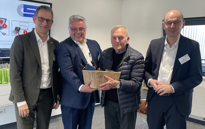 Gruppenfoto mit vier Männern im Anzug einer überreicht einem anderen einen Korb 