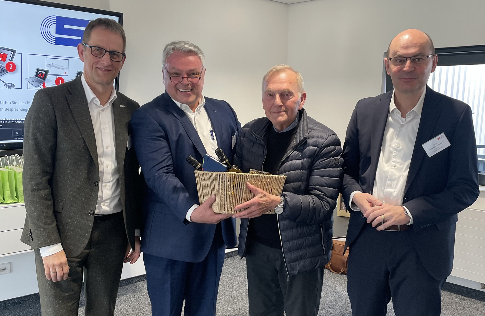 Gruppenfoto mit vier Männern im Anzug einer überreicht einem anderen einen Korb 