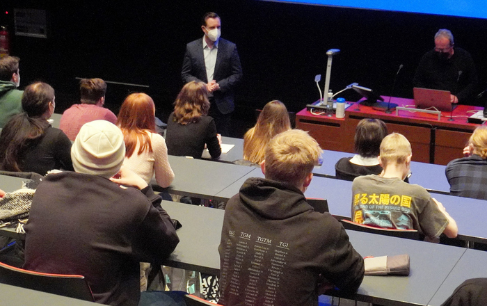 Oliver Schäfer (stehend, links), Prorektor für Studium und Lehre, bei der Begrüßung der neuen Studierenden, die in mehreren aufsteigenden Reihen an Pulten sitzen