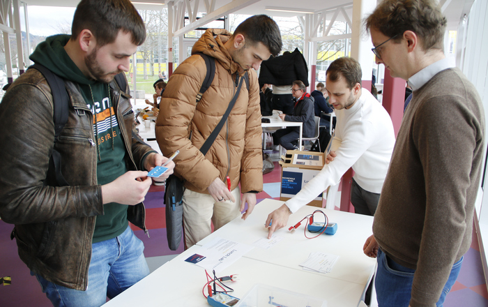 Zwei Studierende stehen in der Mensa an einem Tisch und machen unter den Augen von Prof. Dr. Dominik Giel und Daniel Kehret den Versuch