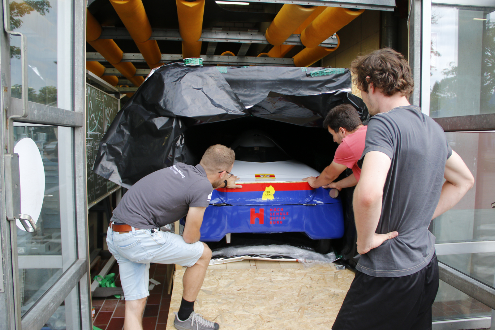 Studierende blicken auf das Auto, das gerade so in die Kiste passt