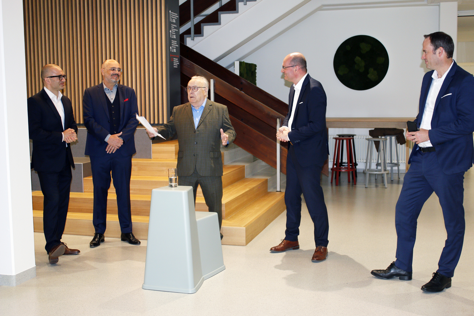 Fünf Herren in Anzügen stehen nebeneinander, einer hält eine Rede die andere hören zu