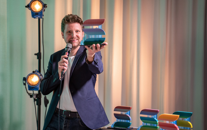 Moderator Kai Wissmann steht vor einem Vorhang und präsentiert den SHORTS-Preis.