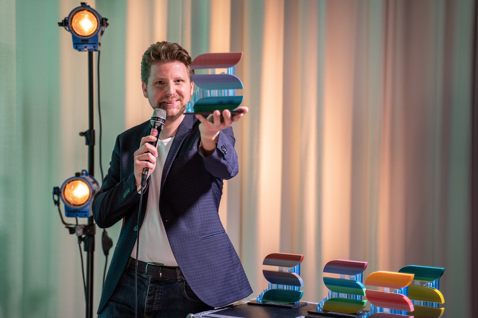 Moderator Kai Wissmann steht vor einem Vorhang und präsentiert den SHORTS-Preis.