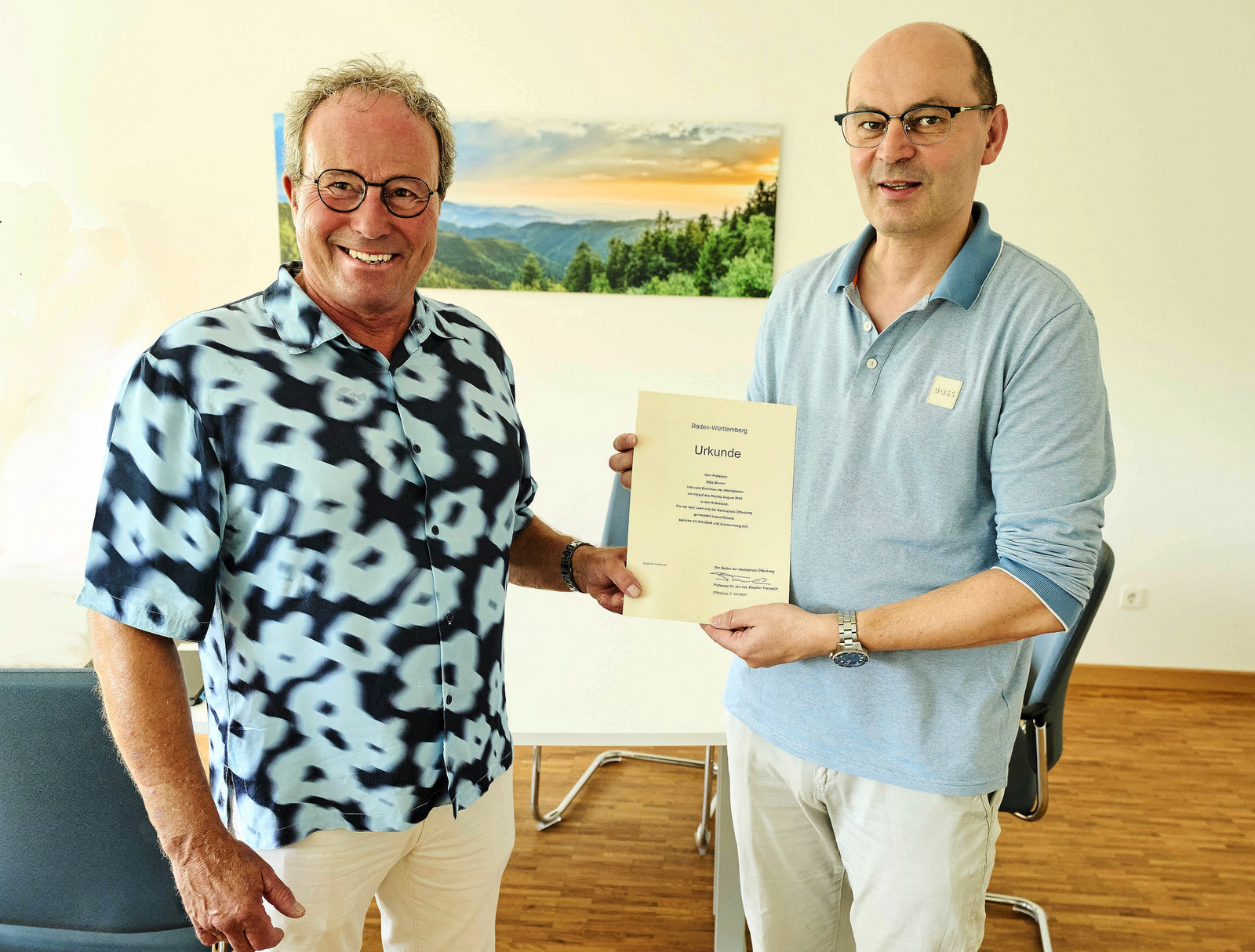 Zwei Männer stehen vor einem Schwarzwaldfoto und halten eine Urkunde zwischen sich