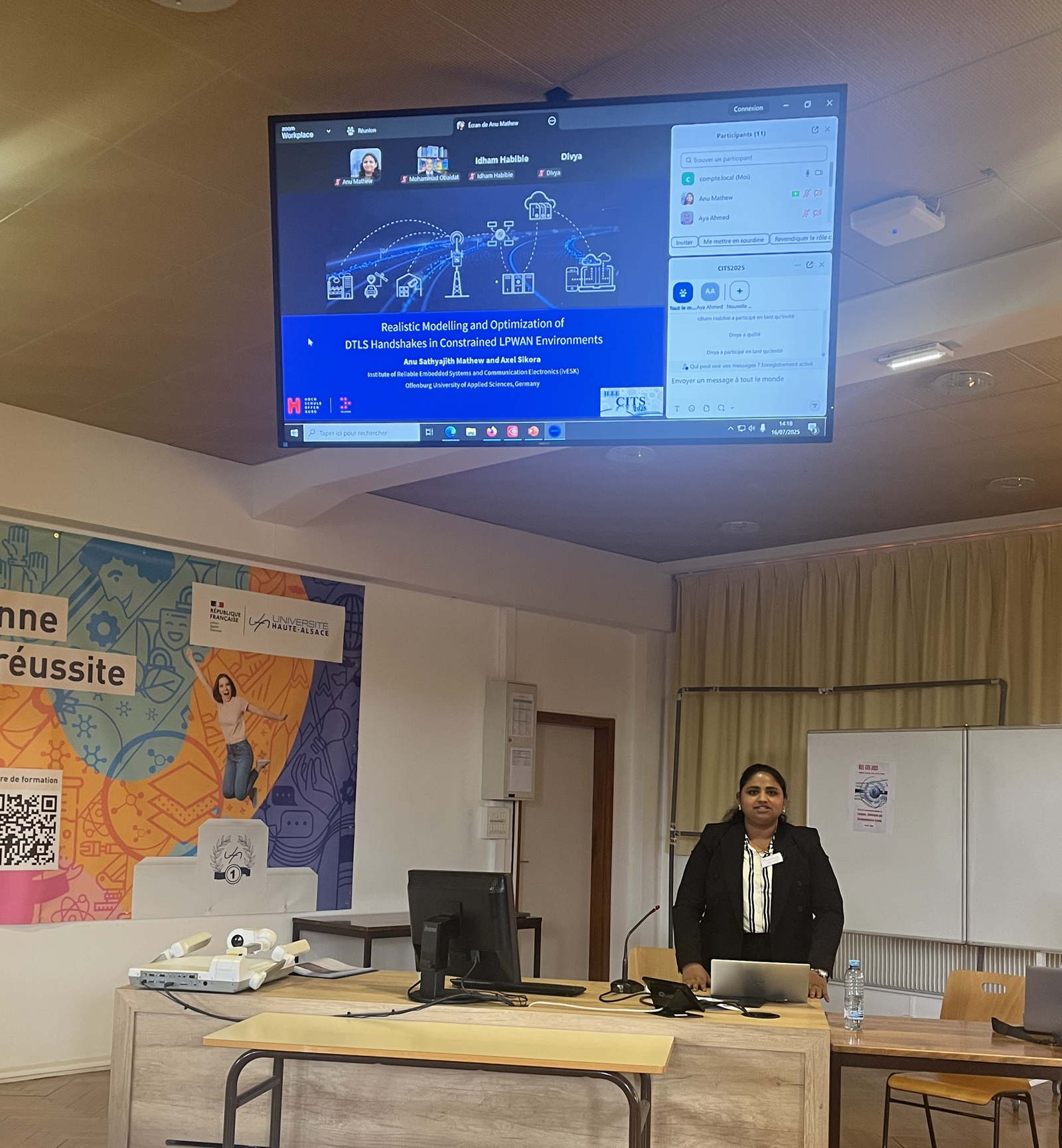 1 Frau an einem Tisch darüber ein großer Bildschirm mit der Präsentation