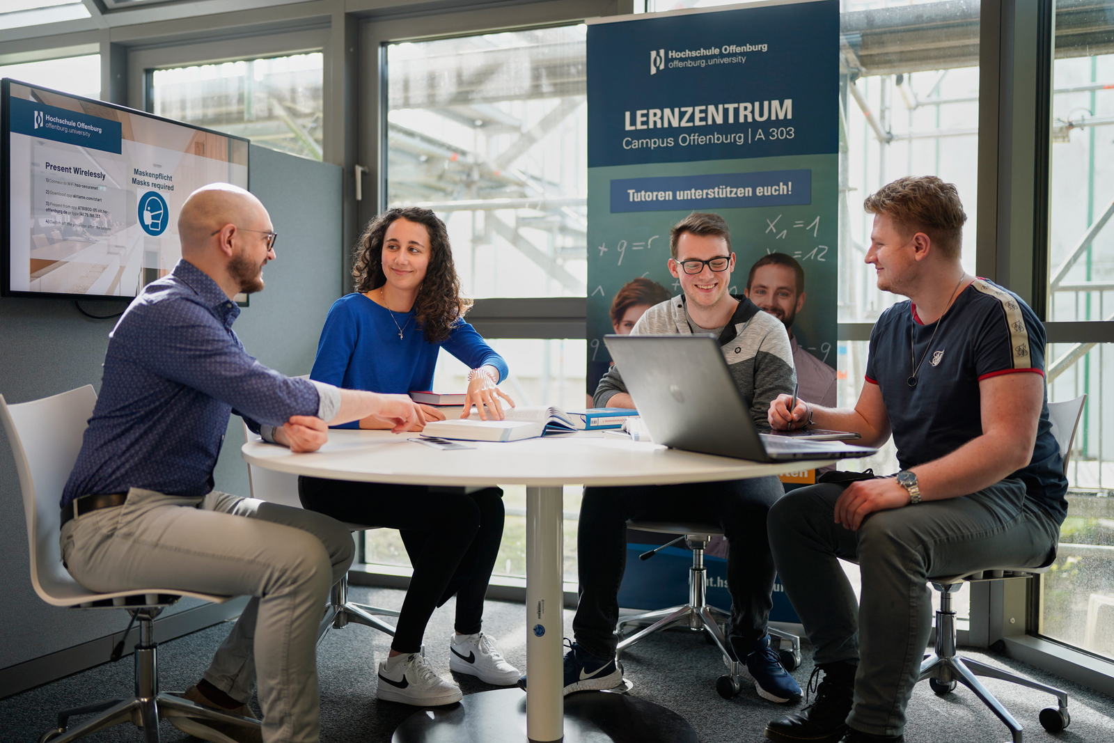 Studierende und Tutor sitzen an einem Tisch in der Bibliothek
