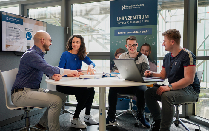 Studierende und Tutor sitzen an einem Tisch in der Bibliothek