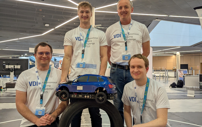 Vier Männer stehen um eine Reifenstapel herum auf dem ein Modellauto steht