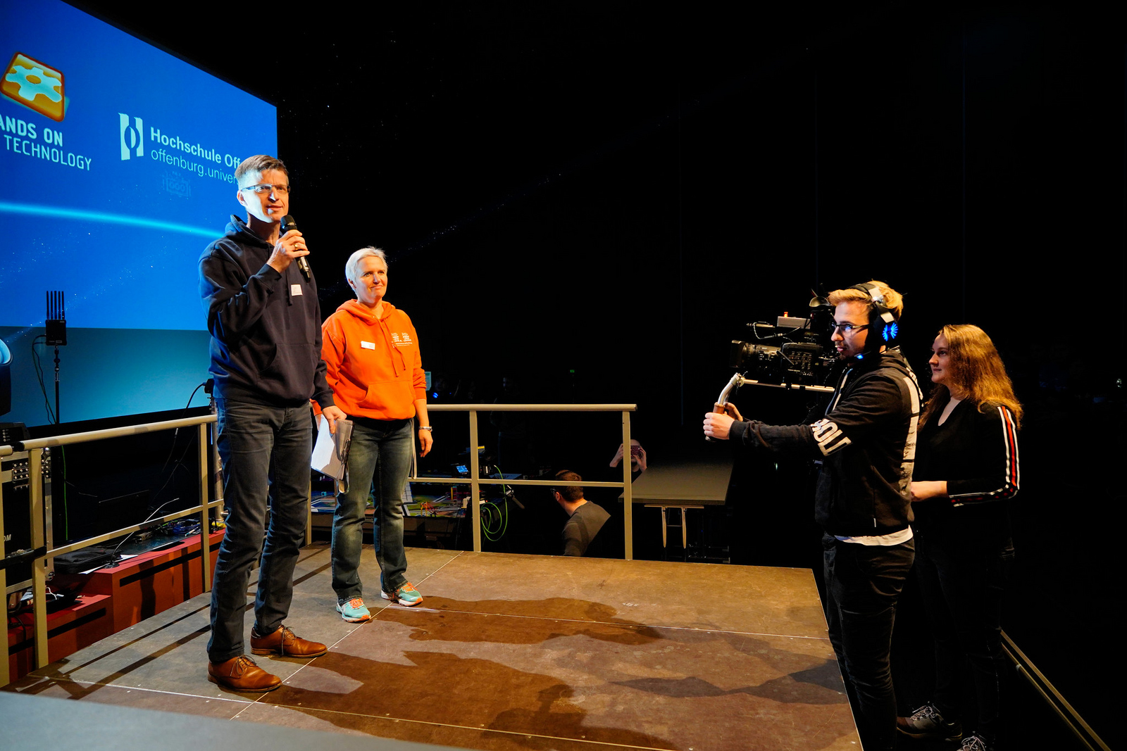 Prof. Dr. Jan Münchenberg, Nicole Diebold und das Mediateam (von links) bei den Vorbereitungen für das FLL-Finale Zentraleuropa auf der Bühne. 