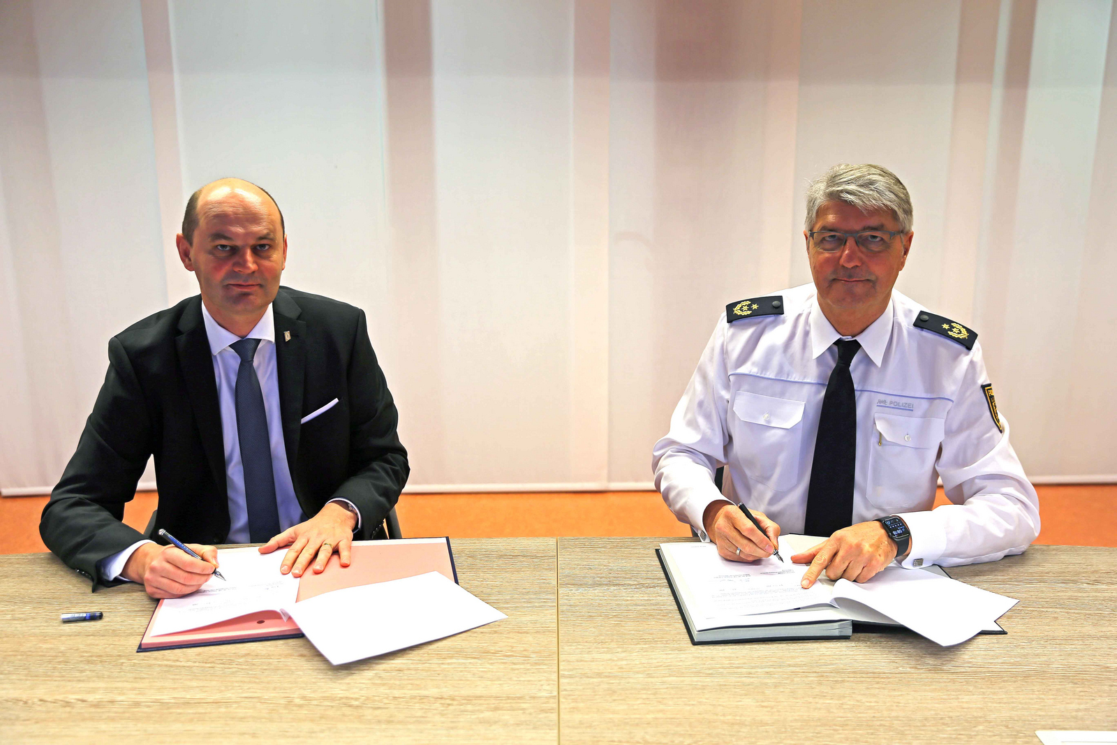 Rektor Prof. Dr. Stephan Trahasch (links) und Polizeipräsident Reinhard Renter (rechts) sitzen bei der Unterzeichnung der Kooperationsvereinbarung an einem Tisch.