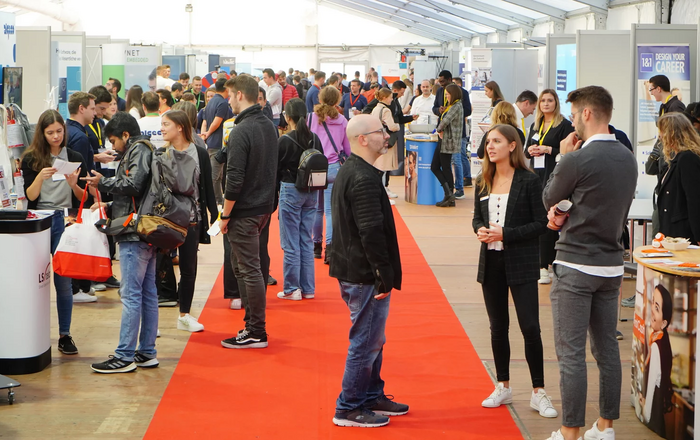 Blick ins Zelt der CAREER-Messe. Links und rechts die Messe-Stände der Unternehmen dazwischen flanieren zahlreiche Studierende, einige sprechen mit Unternehmenvertretern.