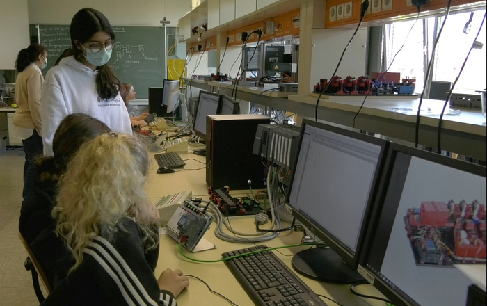 Mädchen sitzen oder stehen an Computern und programmieren