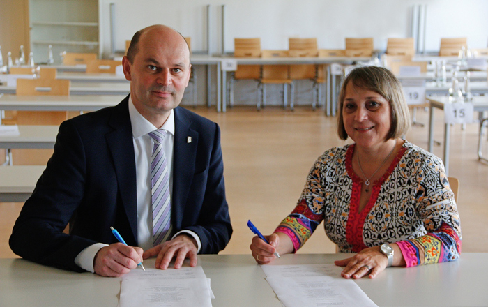 Rektor Prof. Dr. Stephan Trahasch (links) und Schulleiterin Claudia Cassiani (rechts) bei der Unterzeichnung der Partnerschaftsurkunde. 