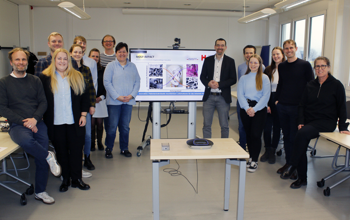 Menschen stehen um einen Bildschirm herum auf dem eine Präsentation des Projekts zu sehen ist