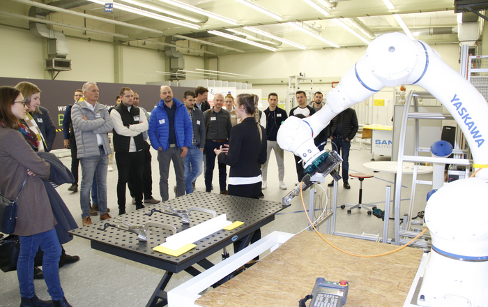 Besuchergruppe schaut Roboter bei der Arbeit zu