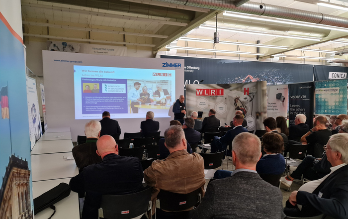 Sitzende Menschen hören einem vor einer Leinwand stehenden Redner zu