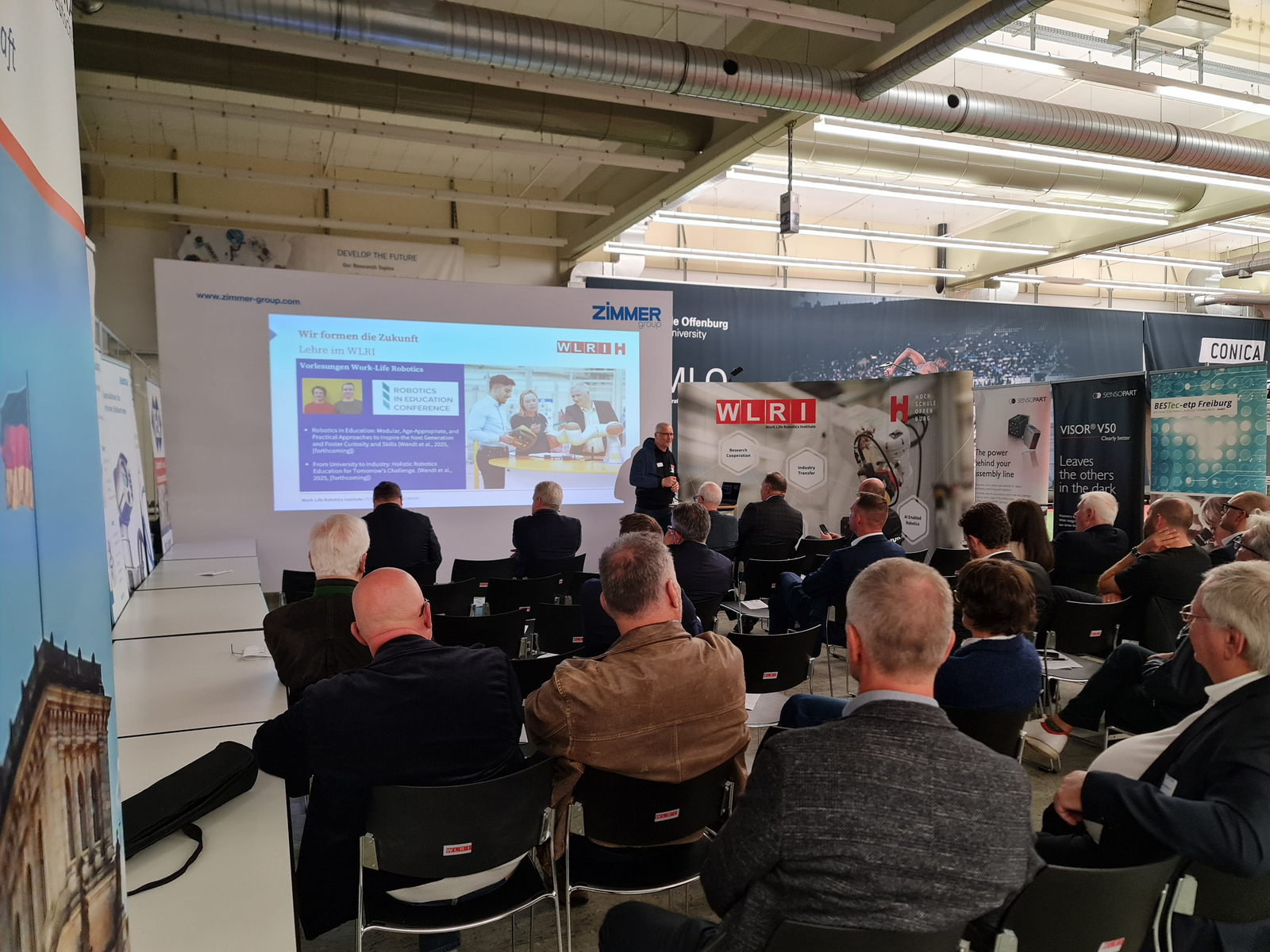 Sitzende Menschen hören einem vor einer Leinwand stehenden Redner zu