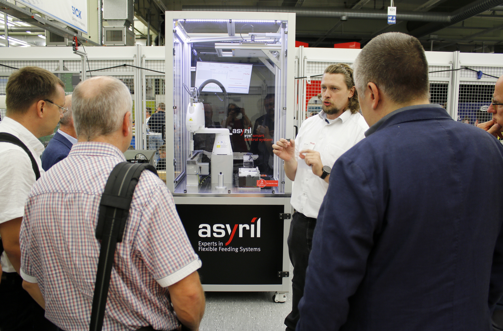 Mehrere Männer stehen vor einem Glaskasten mit einem Roboter. Ein Mann erklärt etwas