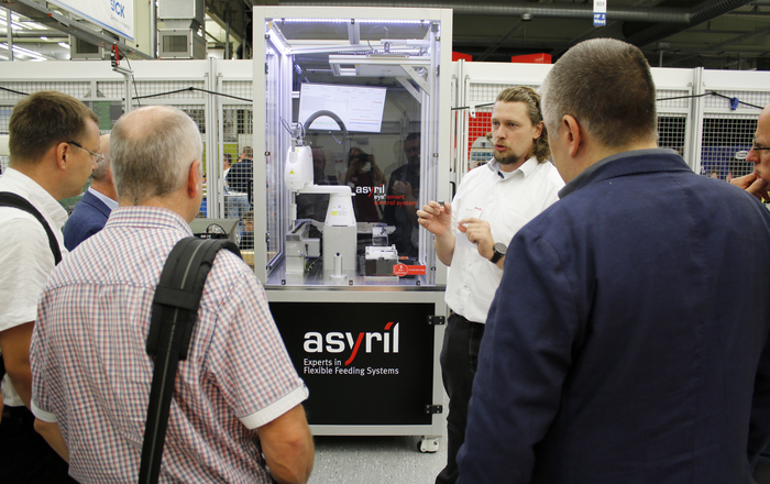 Mehrere Männer stehen vor einem Glaskasten mit einem Roboter. Ein Mann erklärt etwas