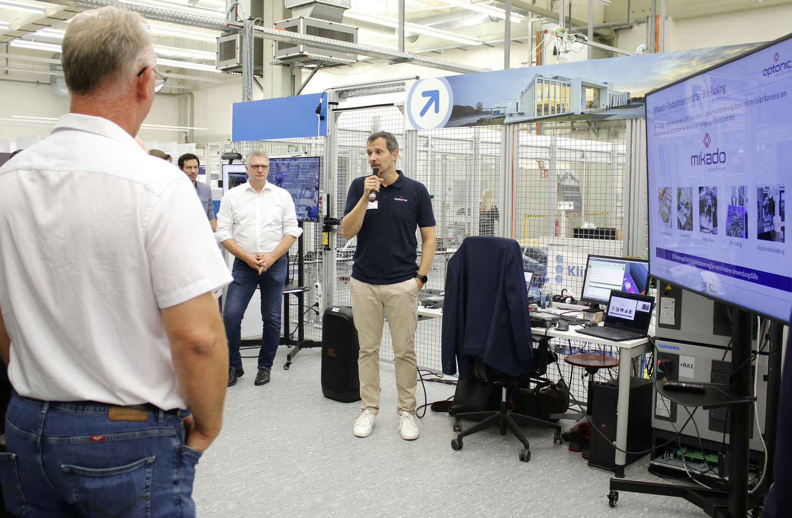 Ein Mann steht neben einem Großbildschirm und erklärt den Umstehenden was darauf zu sehen ist