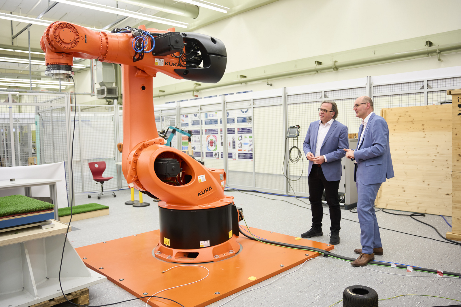 Zwei Männer stehen neben einem großen, orangefarbenen Industrieroboter und unterhalten sich