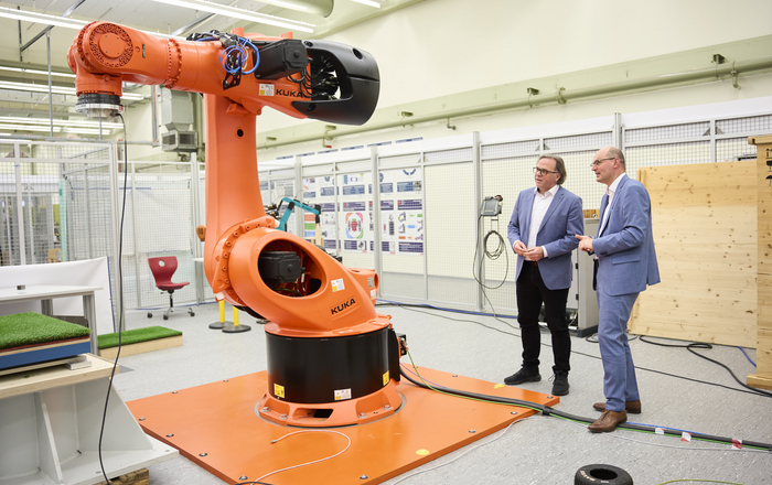 Zwei Männer stehen neben einem großen, orangefarbenen Industrieroboter und unterhalten sich