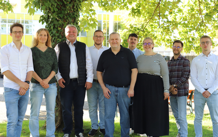 Gruppenfoto des Teams bei Sonnenschein unter einem Baum auf dem Rasen auf dem Campus