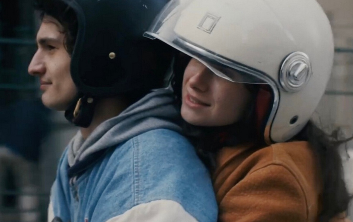 Zwei junge Leute mit Helm die auf einem Scooter fahren, da auf dem Ausschnitt aber nicht zu sehen ist