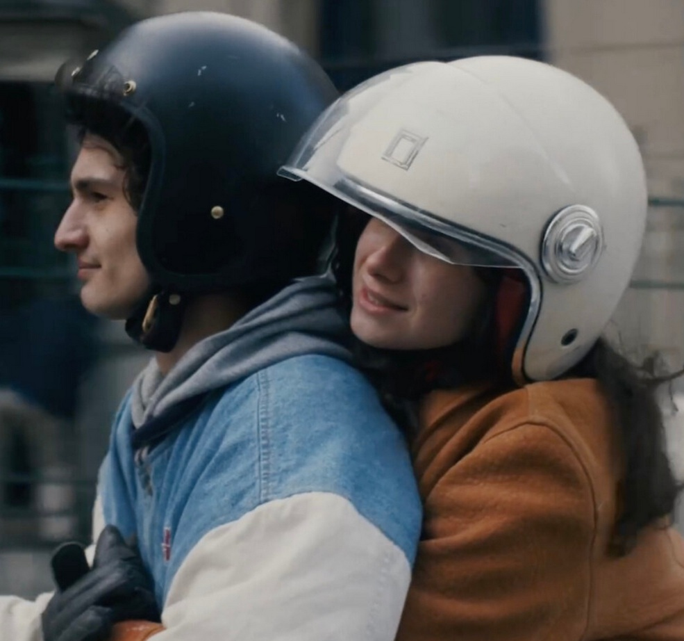 Zwei junge Leute mit Helm die auf einem Scooter fahren, da auf dem Ausschnitt aber nicht zu sehen ist