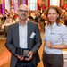 Tobias Hagen und Nicole Ondrusch stehen nebeneinander in einem Saal, im Hintergrund sind verschwommen die sitzenden Konferenzteilnehmer zu erkennen, Tobias HAgen hält die Schatulle mit der medaille in den Händen