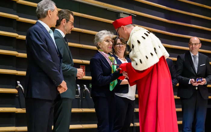 Ein Mann in einer roten Robe mit Hermelinkragen überreicht  mehreren Männern und Frauen eine Medaille