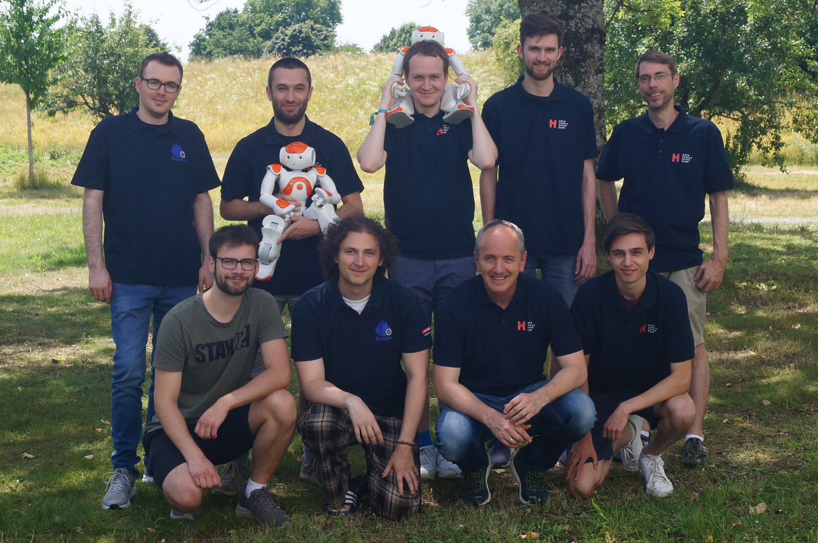 Teamfoto mit Robotern unter einem Baum auf einer Wiese